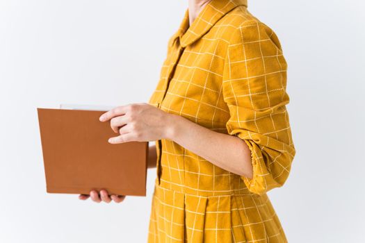 Portrait of a beautiful brunette girl in a yellow retro dress reading a book on white background.