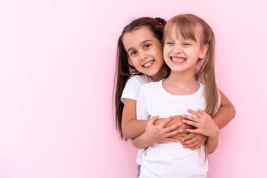 Two little girls hugging each other. Isolated on on a pink background