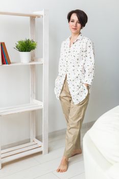 Young attractive woman dressed in beautiful colorful pajama posing as a model in her living room. Comfortable sleepwear, home relaxation and female fashion concept