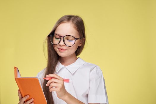 schoolgirl with textbook in hands learning childhood yellow background. High quality photo