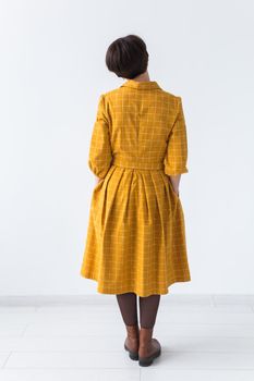 clothing, designer, people concept - back view of attractive woman in a yellow dress posing on white room