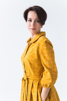 Portrait of a happy young woman in bright yellow dress over white room background. Beauty, fashion concept