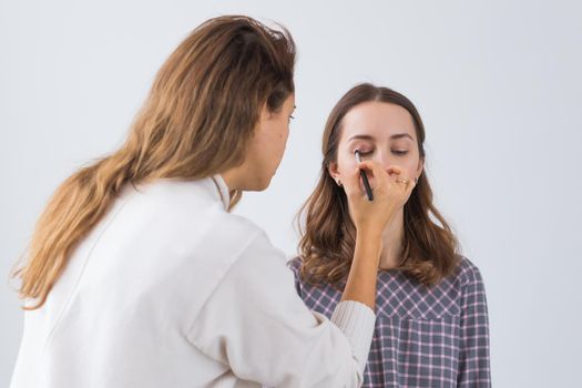 Beauty and cosmetics concept - Makeup artist doing professional make up of young woman.