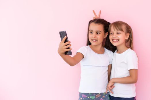 two little girls with a smartphone on a pink background