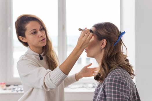 Beauty and cosmetics concept - Makeup artist doing professional make up of young woman.