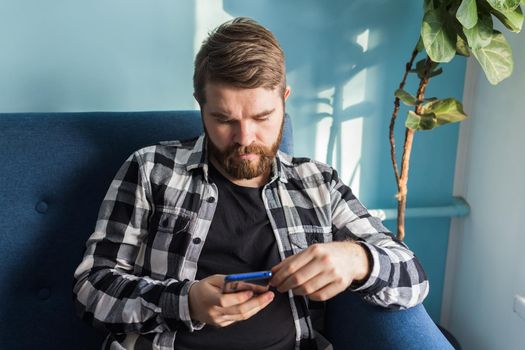 Technologies and leisure concept - Cheerful man sitting on the couch using his smartphone at home in living room.