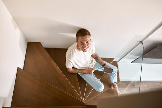 Relaxing happy caucasian man on the minimalistic stairs in modern light apartment