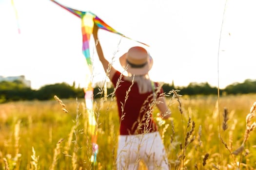 Happy young woman running with a kite on a glade at sunset in summer