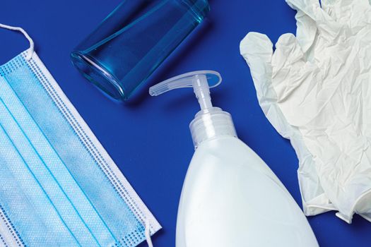 Coronavirus prevention. Facial mask, gloves, soap and sanitizer on blue background close up