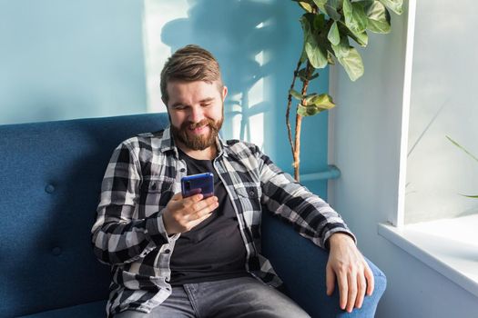 Man playing online games with a smart phone sitting on a couch at home