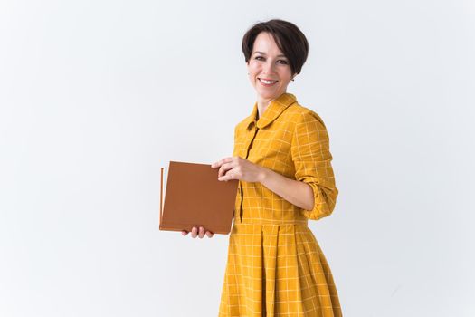 Portrait of a beautiful brunette girl in a yellow retro dress reading a book on white background.