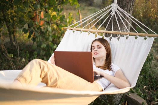 woman outdoors with laptop lies in hammock leisure technology. High quality photo