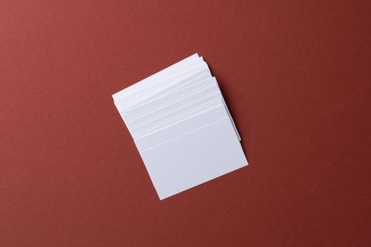 Blank white business cards on burgundy paper background, top view