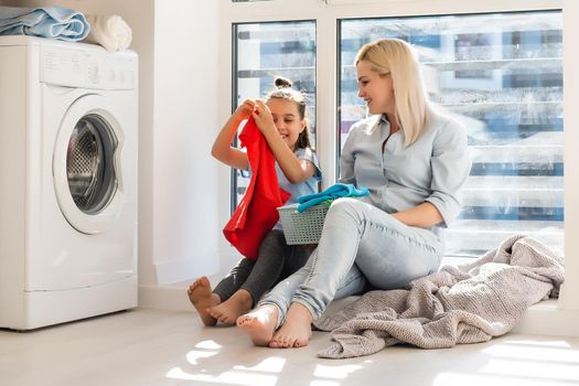 Young housewife and little girl doing laundry together