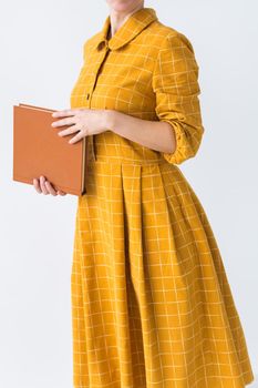 Portrait of a beautiful brunette girl in a yellow retro dress reading a book on white background.