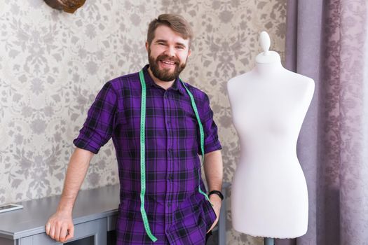 Man tailor seamstress workshop stylish male model clothes designer measuring tape on neck posing next to the mannequin in his home creative clothes design.