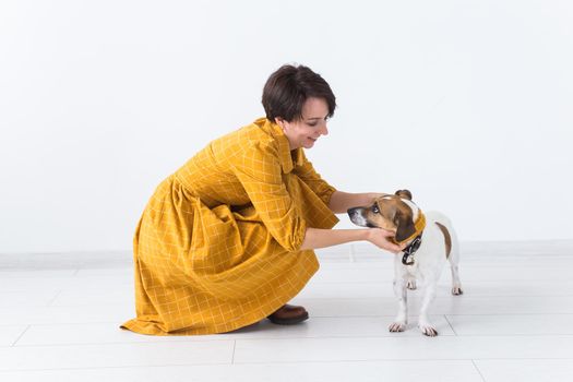 Cheerful young woman posing in a yellow dress with her beloved dog Jack Russell Terrier standing on a white background. The concept of casual wear