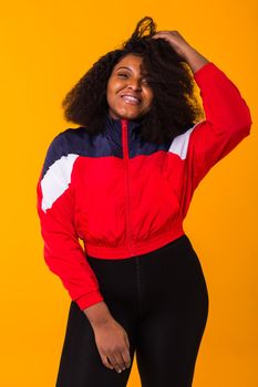 Funny curly african american girl dressed in the red sports jacket in the studio on yellow background. Fashion and people.