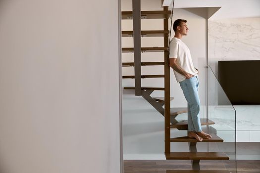 Relaxing happy caucasian man on the minimalistic stairs in modern light apartment