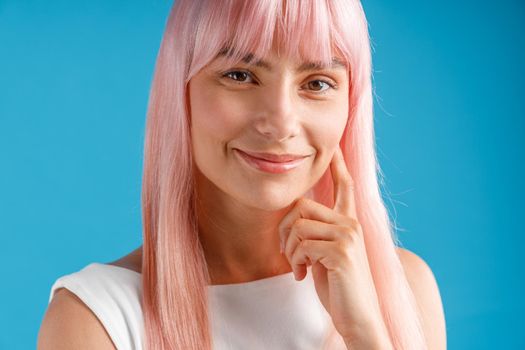 Portrait of beautiful young woman with pink hair smiling at camera, posing isolated over blue studio background. Emotions, lifestyle concept