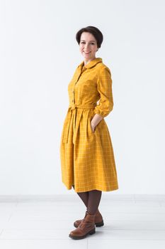 Portrait of a happy young woman in bright yellow dress over white room background. Beauty, fashion concept