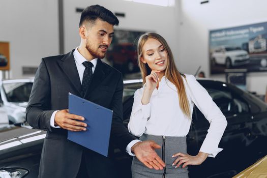 Man car dealer showing a woman buyer a new car in car salon