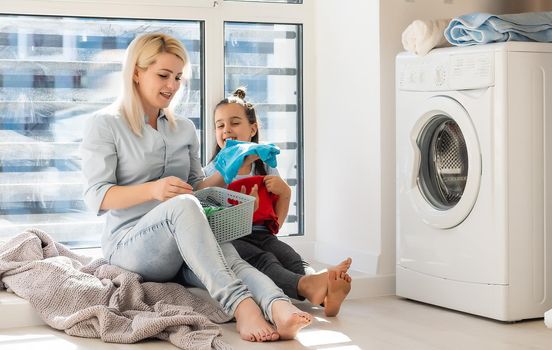 family mother and child girl little helper in laundry room near washing machine and dirty clothes