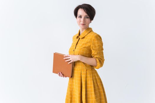 Portrait of a beautiful brunette girl in a yellow retro dress reading a book on white background.