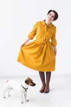 Cheerful young woman posing in a yellow dress with her beloved dog Jack Russell Terrier standing on a white background. The concept of casual wear