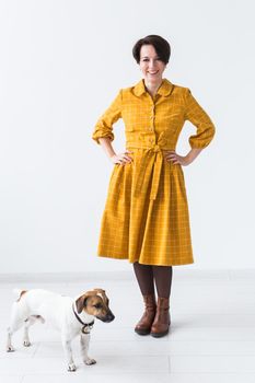 Cheerful young woman posing in a yellow dress with her beloved dog Jack Russell Terrier standing on a white background. The concept of casual wear