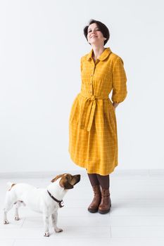 Cheerful young woman posing in a yellow dress with her beloved dog Jack Russell Terrier standing on a white background. The concept of casual wear