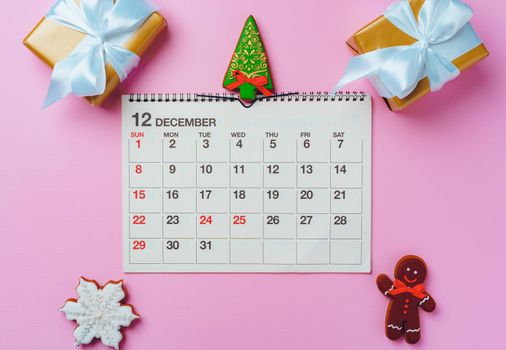 Calendar page of december with festive decorations on pink background, top view