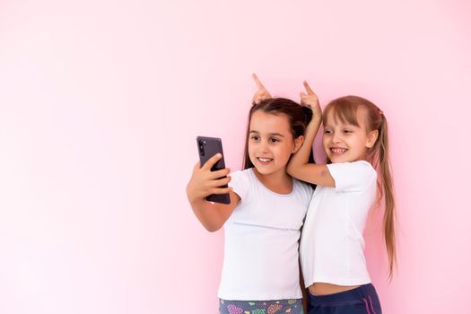 Two little girls playing with smartphones on a pink background