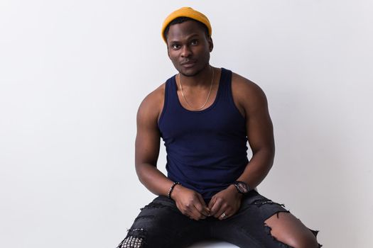 Portrait of sexy trendy african man sitting on a chair on white background. Youth concept