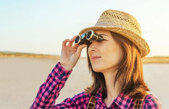 Beautiful young hipster girl looks through binoculars