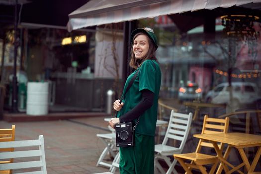 Happy young caucasian lady in green dress is walking near cozy cafe