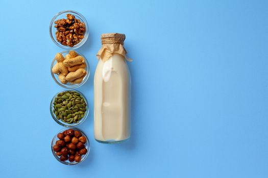 Vegetable milk concept with milk bottle and bowls with grains and nuts on blue background top view