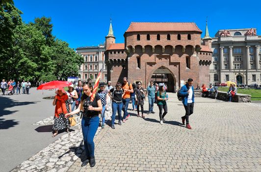 Krakow, Poland - May 20, 2019: The Krakow Barbican - a fortified outpost. It is a historic gateway leading into the Old Town of Krakow, Poland. Group of tourists on excursions near Krakow Barbican