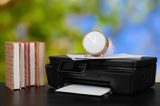 Stack of books and home printer against blurred background, close up