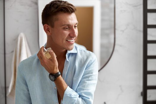 Photo of adult caucasian beautiful man in front of mirror in light modern bathroom