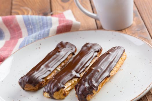 Chocolate eclairs on white plate on wooden table close up