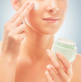 Unrecognizable woman applies moisturizer cream on face, concept of skincare