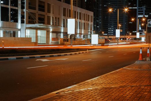 Empty asphalt road with modern buildings at night in Dubai, UAE