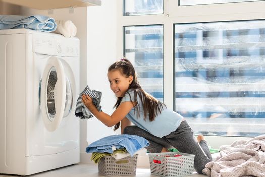 Beautiful child girl little helper is having fun and playing while doing laundry at home.