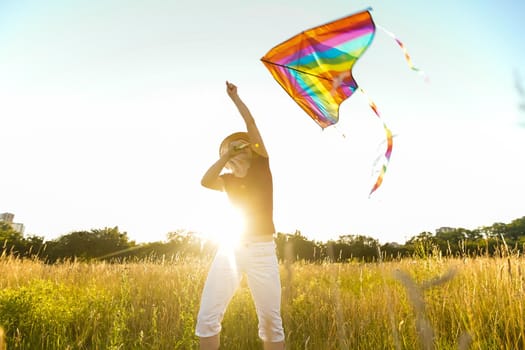 Happy young woman running with a kite on a glade at sunset in summer