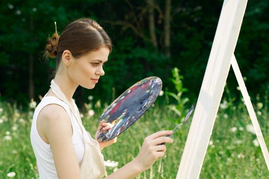 woman artist outdoors with palette of paints paints a picture. High quality photo