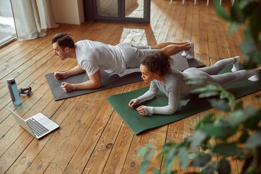 Top view of athletic man and woman in plank position in front of notebook during workout