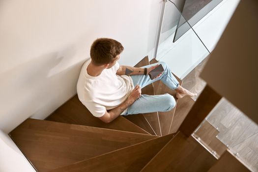 Relaxing happy caucasian man on the minimalistic stairs in modern light apartment