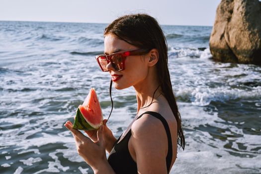 woman in black swimsuit with watermelon by the ocean. High quality photo