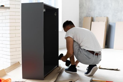Assembling new wooden furniture by hand in room. Man putting together new furniture.